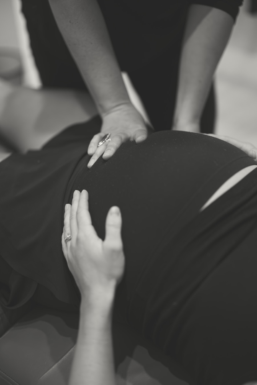 Gentle hands checking a pregnant belly during an adjustment, in black and white